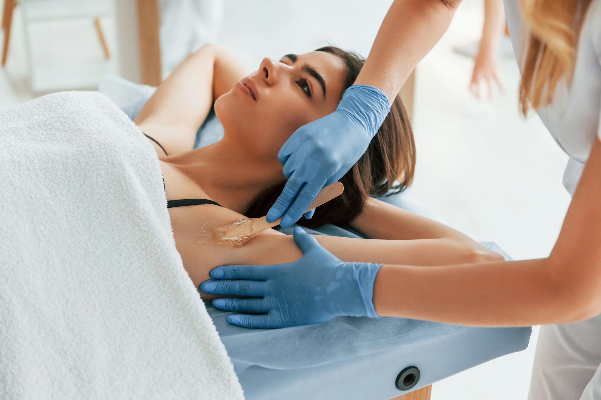 Putting cream on the armpits. Woman is having sugaring procedure in the clinic by female doctor